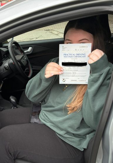 Well done Abbie A person sitting in a car holding a document partially obscuring their face.